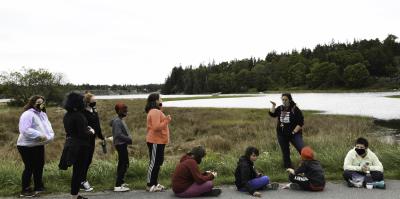 nine students outside along a roadside near a tidal marsh listening to teacher talk about sea level rise