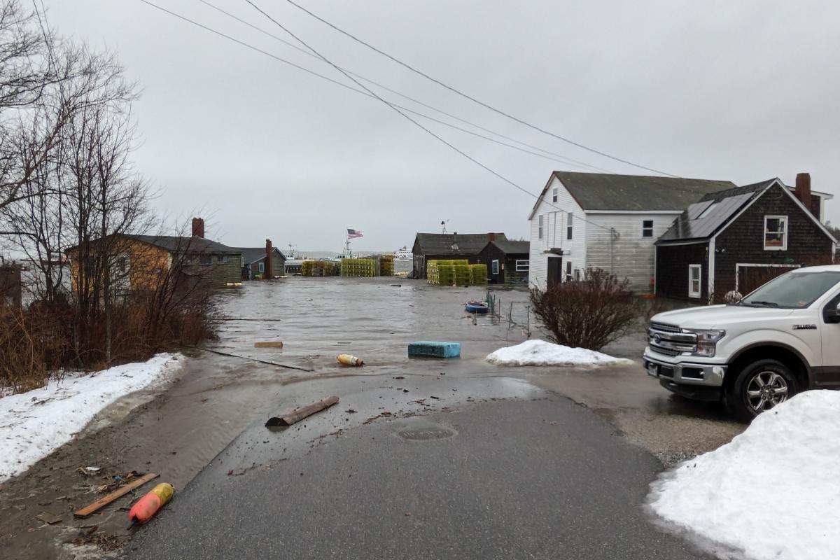 coastal street with flooded lane and flood debris, buildings in the background, gray overcast sky